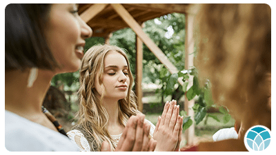 Two women are praying together outside in a forest.