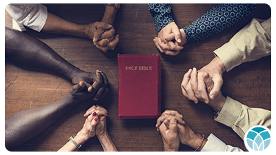 A group of people holding hands around the bible.